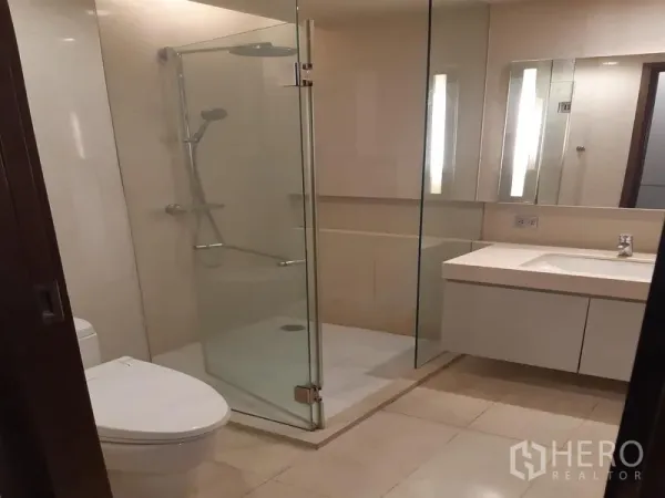 公寓 出租在Watthana, Bangkok - 现代浴室，透明玻璃淋浴间、马桶和带镜子的洗手台。
