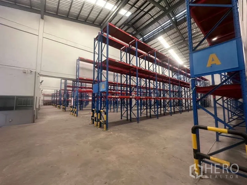 Warehouse for rent in Mueang Samut Prakan, Samut Prakan - Aisles between labeled pallet racks under a steel roof, ready for logistics operations.