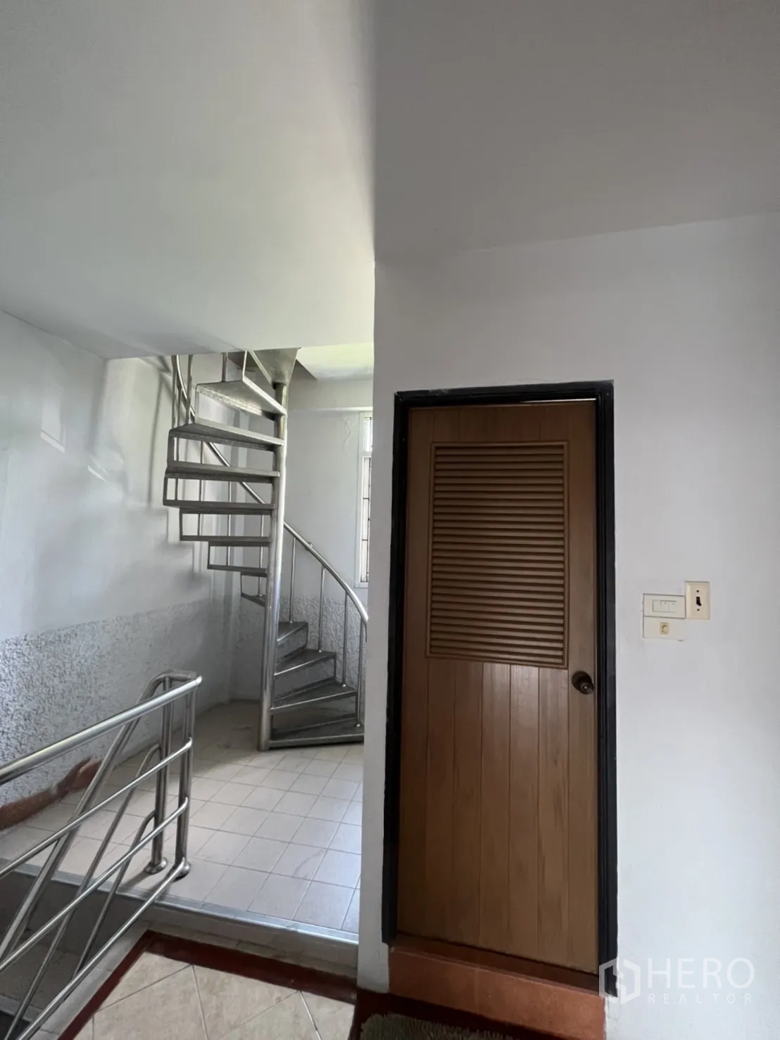 Shophouse for rent in Khlong Toei, Bangkok - Landing area with stainless-steel spiral staircase beside a wooden door.