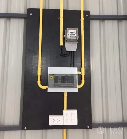 Warehouse for rent in Khan Na Yao, Bangkok - Electrical panel with meter, conduits, and outlets mounted on the wall.
