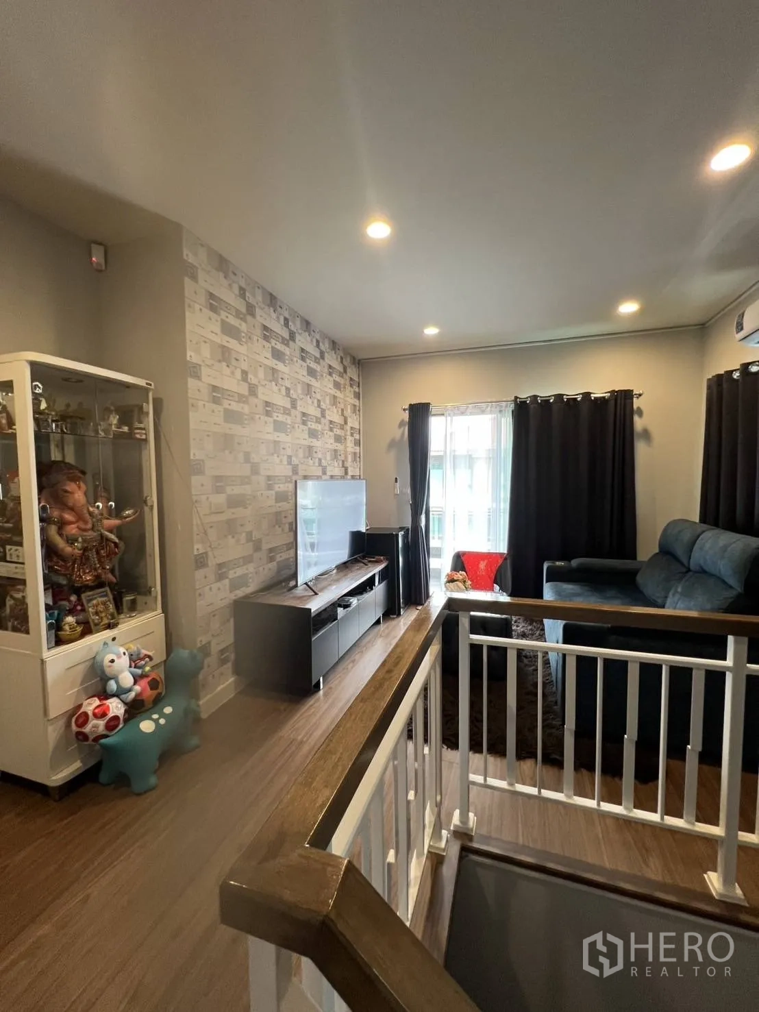 Detached House for rent or sale in Lam Luk Ka, Pathum Thani - Upstairs family lounge by the stair landing with sofa, TV console, and display cabinet.