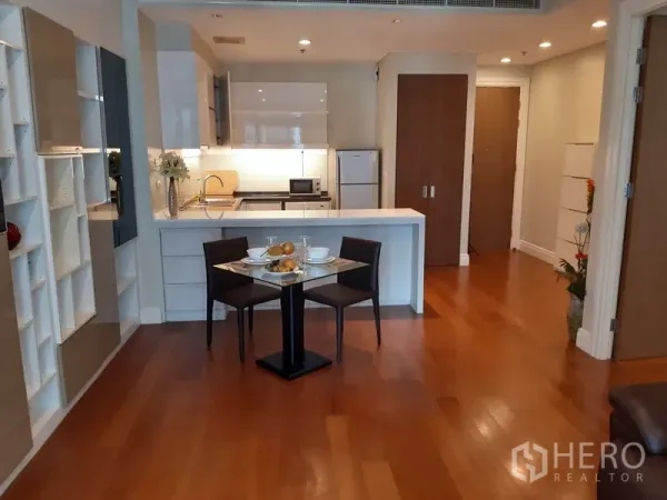 Condominium for rent in Khlong Toei, Bangkok - Open-plan dining and white kitchen with peninsula counter, modern cabinetry and table set for two in a Bangkok condo.