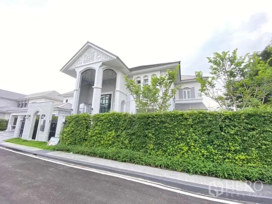 Detached House for rent or sale in Lat Krabang, Bangkok - Corner facade of a luxury house with gated entry and trimmed hedges.