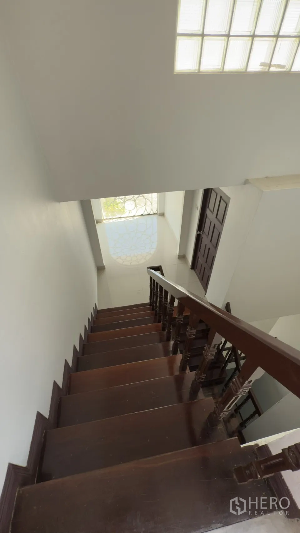 联排别墅 for rent in Watthana, Bangkok - 木质楼梯向下通往前厅，尽头有花纹拱形窗。