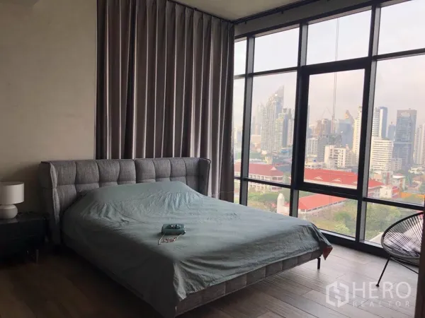Condominium for sale in Watthana, Bangkok - Master bedroom with upholstered bed and full-height windows showcasing wide city skyline views.