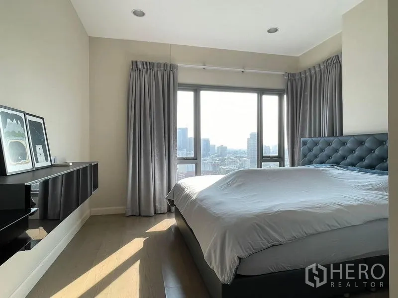 Condominium for sale in Khlong Toei, Bangkok - Master bedroom with large windows, upholstered headboard and skyline outlook.