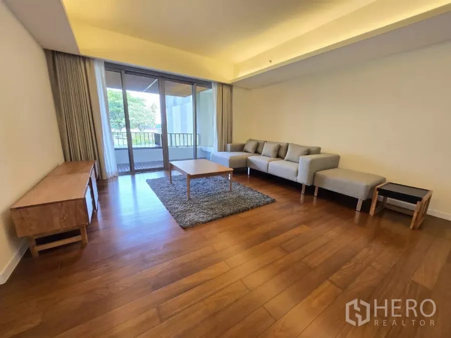 公寓 出租在Yan Nawa, Bangkok - 采光充足的客厅，L形灰色沙发、木地板，落地移门通往带花园景的阳台。