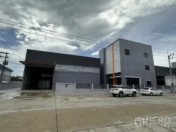 Factory for rent or sale in Lam Luk Ka, Pathum Thani - Front elevation of modern grey warehouse and office with parking spaces and perimeter fence.