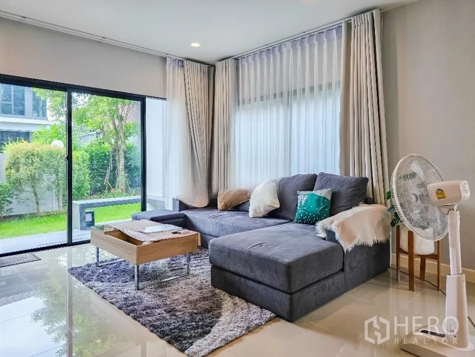 Detached House for sale in Lam Luk Ka, Pathum Thani - Lounge facing the garden with floor-to-ceiling windows and a sliding glass door.