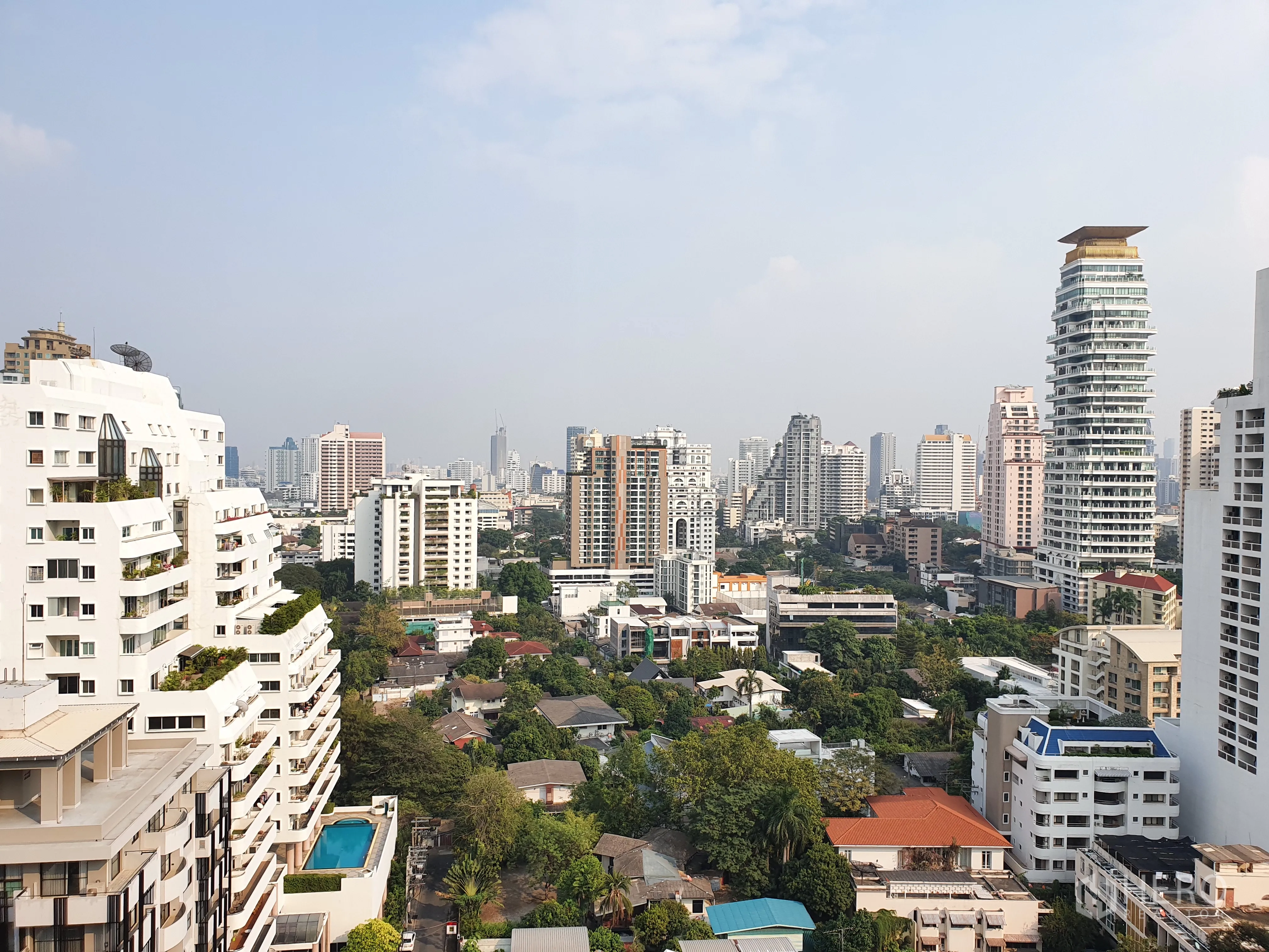 Condominium for rent in Watthana, Bangkok - High-floor balcony view over the Watthana skyline with modern towers and leafy low-rise streets.