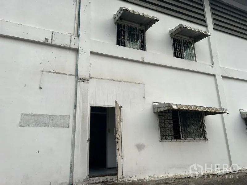 货栈 出租在Bang Sao Thong, Samut Prakan - 外墙带防盗窗与侧门的仓库立面。