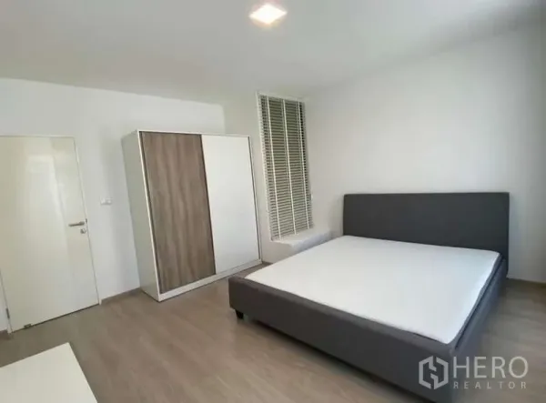 Townhouse for rent in Bang Phli, Samut Prakan - Bright master bedroom with gray upholstered bed, wood wardrobe and tall window blinds.