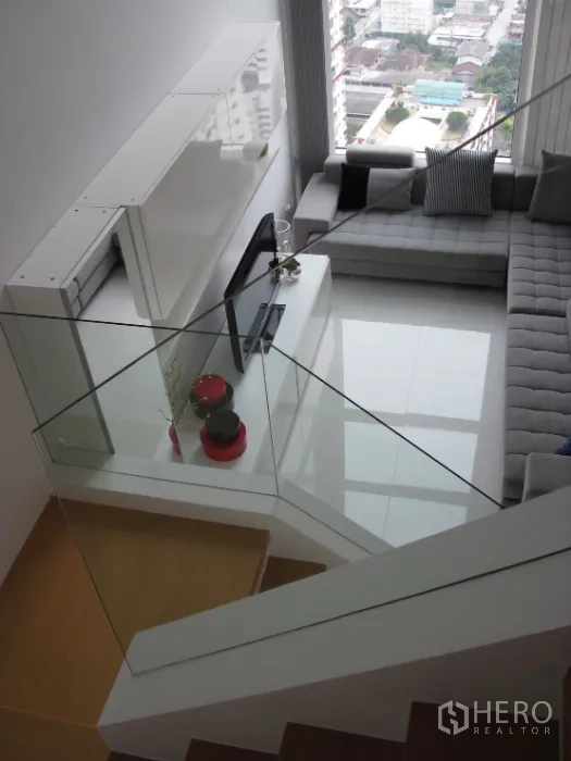 Condominium for rent in Ratchathewi, Bangkok - View from staircase to airy living room with sectional sofa, TV unit and tall windows.