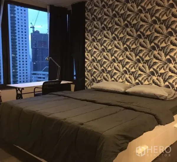 公寓 出租在Watthana, Bangkok - 卧室配特色壁纸、大床与书桌，窗外可见城市景观。