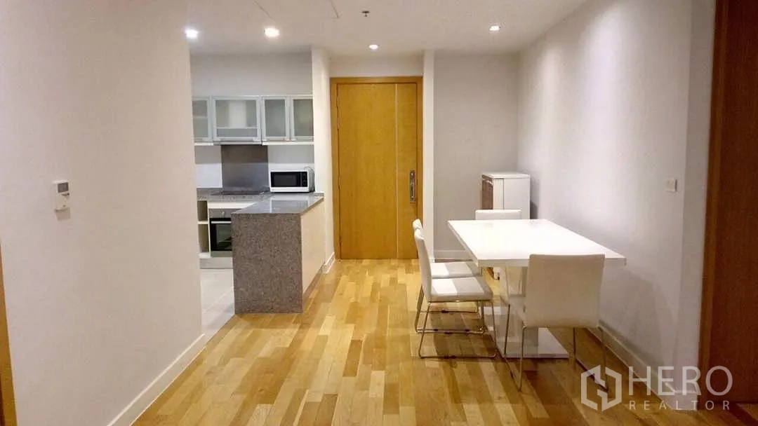 Condominium for rent or sale in Khlong Toei, Bangkok - Open-plan dining area with white table beside a modern kitchen featuring a granite island and built-in appliances.