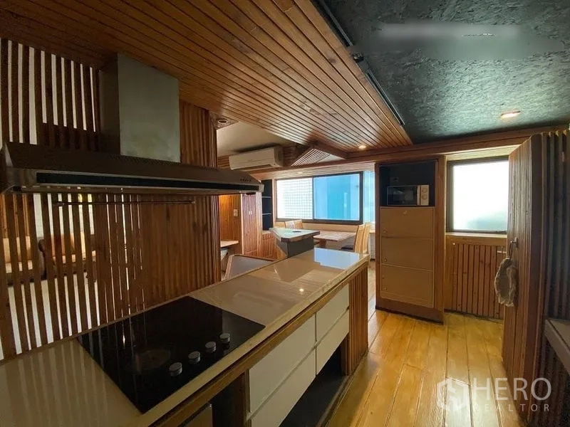 Condominium for rent or sale in Suan Luang, Bangkok - Modern kitchen with island, cooktop, range hood and warm wood ceiling and cabinetry.