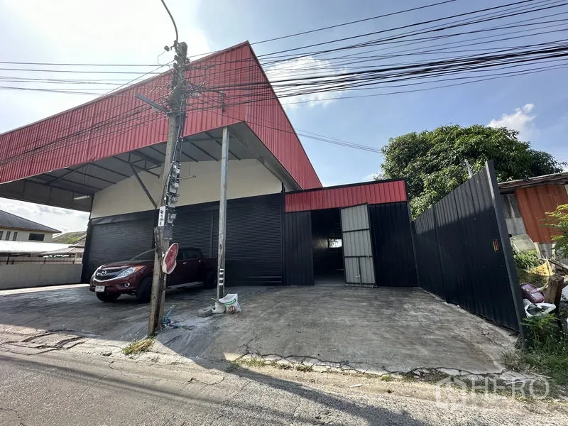 Warehouse for rent in Lat Phrao, Bangkok - Angled exterior of the warehouse showing gated side entrance, black metal fence and a spacious concrete forecourt.