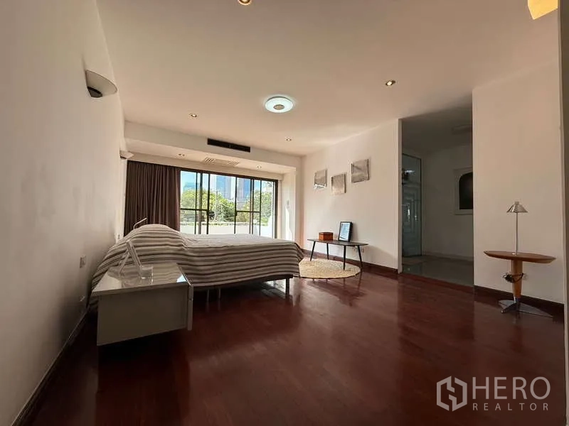 Townhouse for rent in Khlong Toei, Bangkok - Spacious master bedroom with wood floors and sliding glass doors to a balcony.