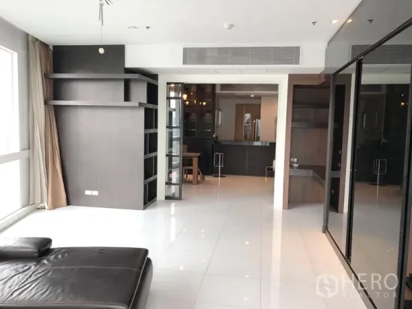 Condominium for rent in Khlong Toei, Bangkok - Open-plan lounge with built-in media wall and shelving leading toward the kitchen in a modern condo.