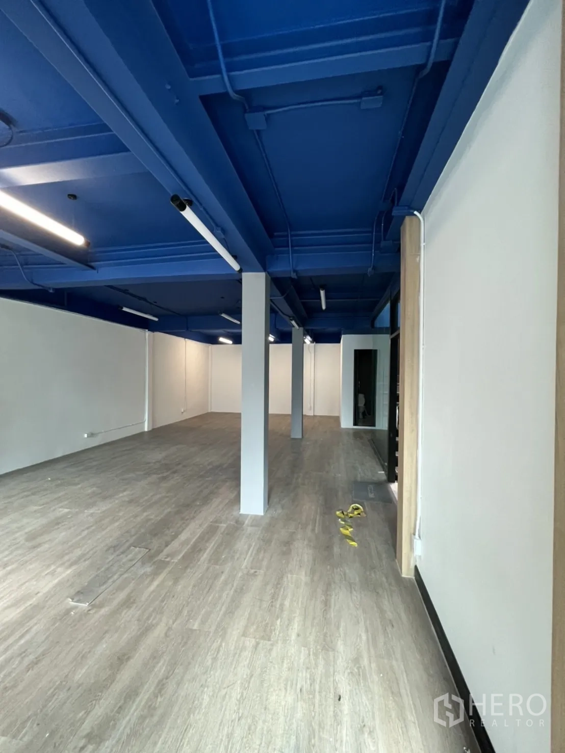 办公空间 出租在Watthana, Bangkok - 宽阔办公通道，立柱分隔，蓝色工业风顶与乙烯基地面。