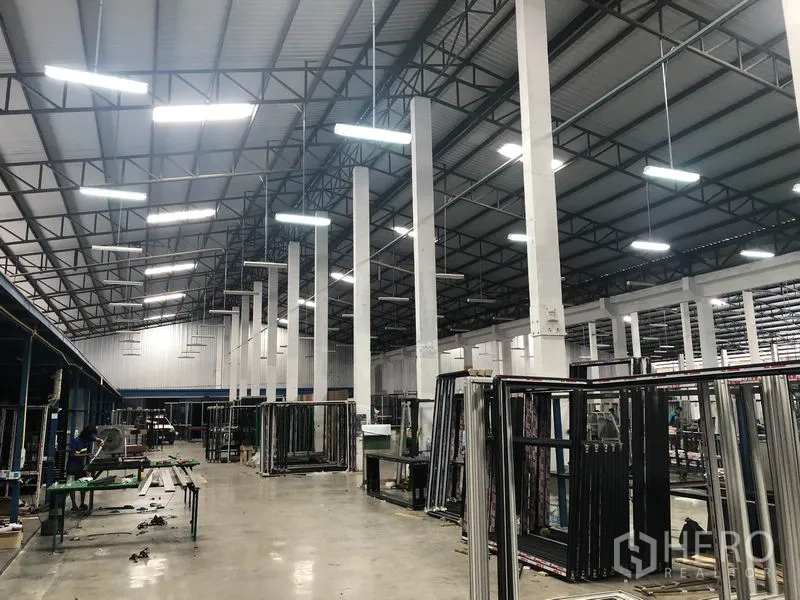 货栈 出租在Nonthaburi - 明亮工业大厅，钢桁架屋顶与悬挂灯具和作业区