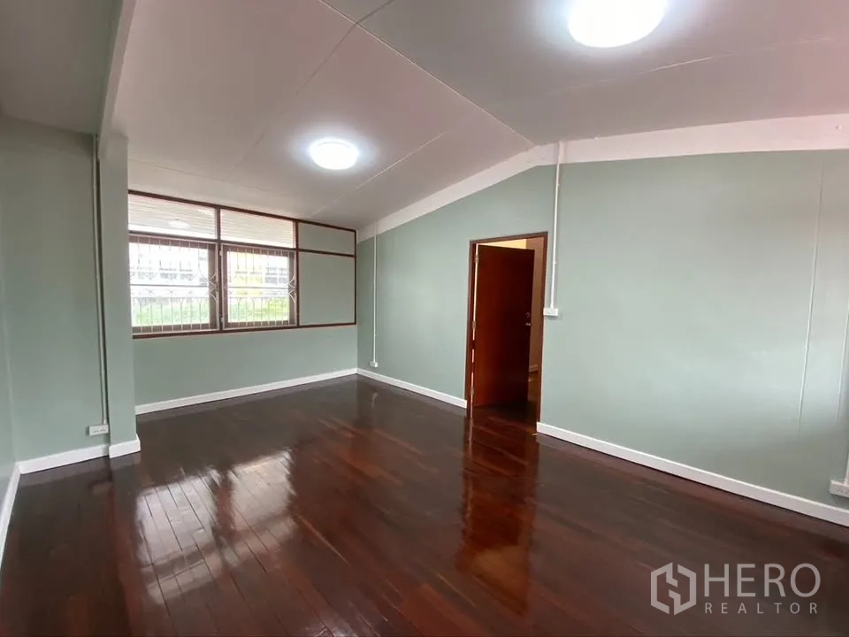 Detached House for rent in Suan Luang, Bangkok - Large room with dark wood floors, green walls, and wide windows.