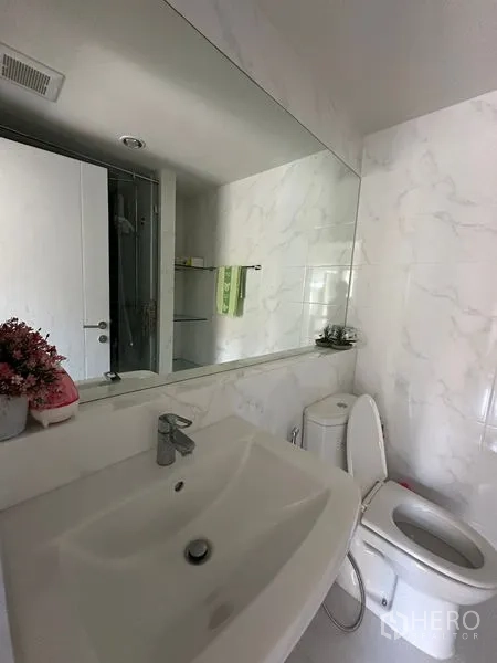 公寓 出售在Khlong Toei, Bangkok - 浴室配大镜面、台盆与坐厕，墙面为大理石纹瓷砖。