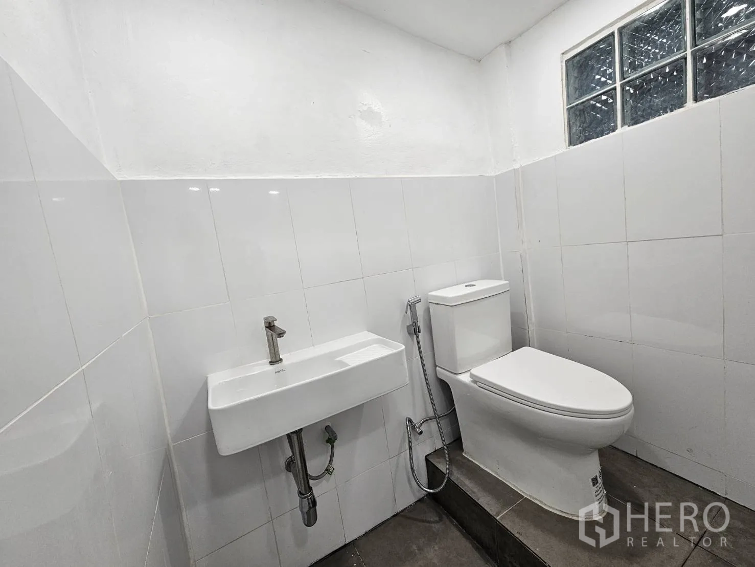 Home Office for rent in Khlong Toei, Bangkok - Renovated bathroom with white tiles, wall-mounted sink and toilet.