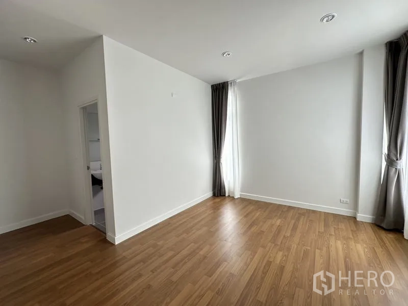 Detached House for sale in Lam Luk Ka, Pathum Thani - Bedroom with wood floors, curtains and a door to the bathroom.