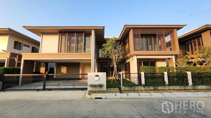 Detached House for rent or sale in Bang Kapi, Bangkok - Front elevation of the two‑storey home with carport and neatly trimmed hedge.