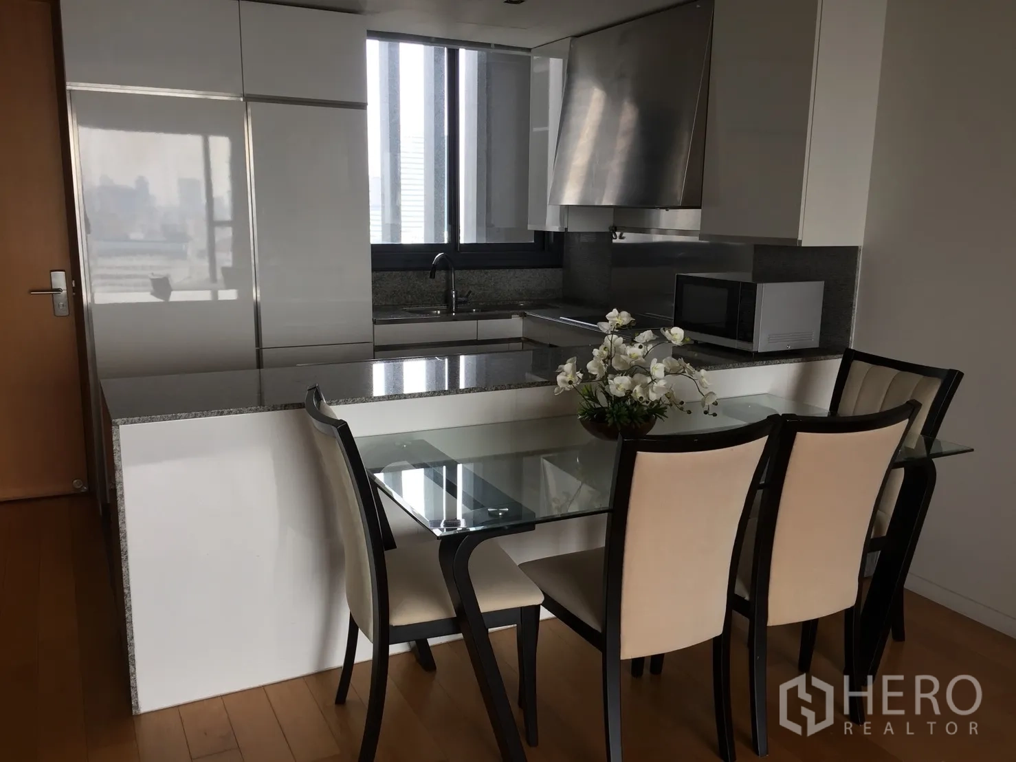 Condominium for rent or sale in Sathon, Bangkok - Modern kitchen with granite countertop, white cabinets and glass dining table for four.