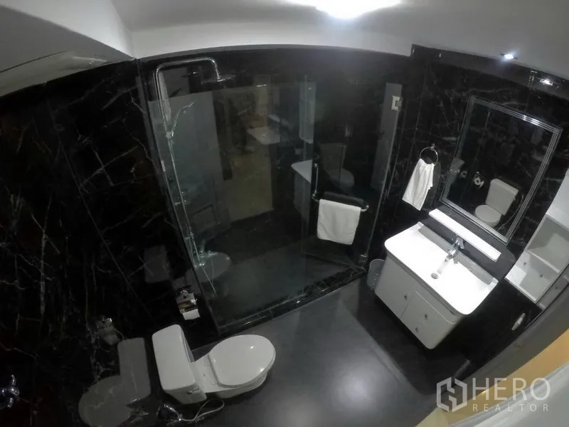 Condominium for rent in Watthana, Bangkok - Contemporary bathroom with black marble tiles and a glass-enclosed shower.