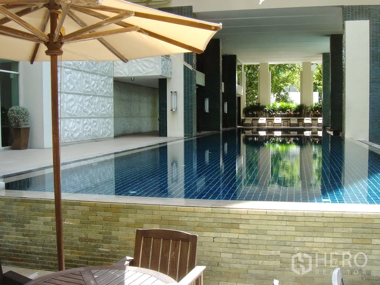 公寓 出租或出售在Pathum Wan, Bangkok - 公寓配套的半室内游泳池，设躺椅与绿植休闲区。