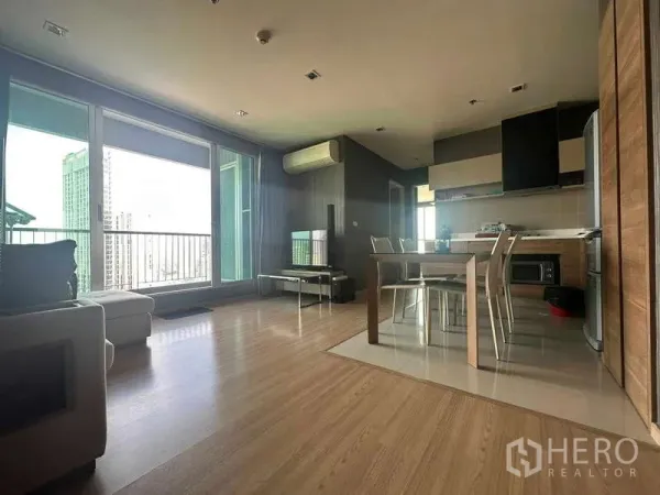 Condominium for sale in Phaya Thai, Bangkok - Open‑plan living and kitchen with floor‑to‑ceiling windows, balcony, and skyline view at Rhythm Phahol‑Ari.