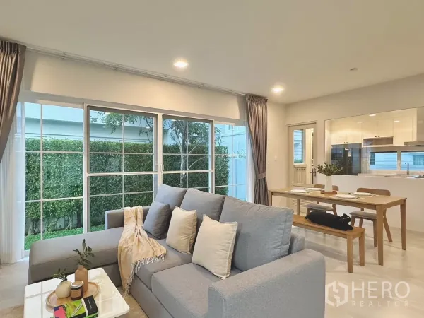 Detached House for rent in Bang Phli, Samut Prakan - Cozy lounge with gray L-shaped sofa beside windows, adjacent to dining and kitchen.