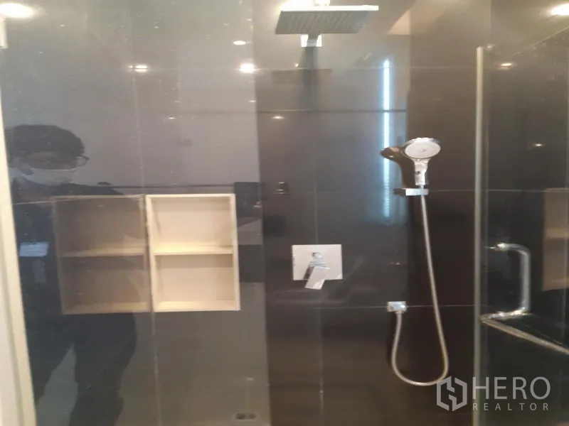 Condominium for rent in Khlong Toei, Bangkok - Glass-enclosed shower with rainfall and handheld heads against dark tiled walls.