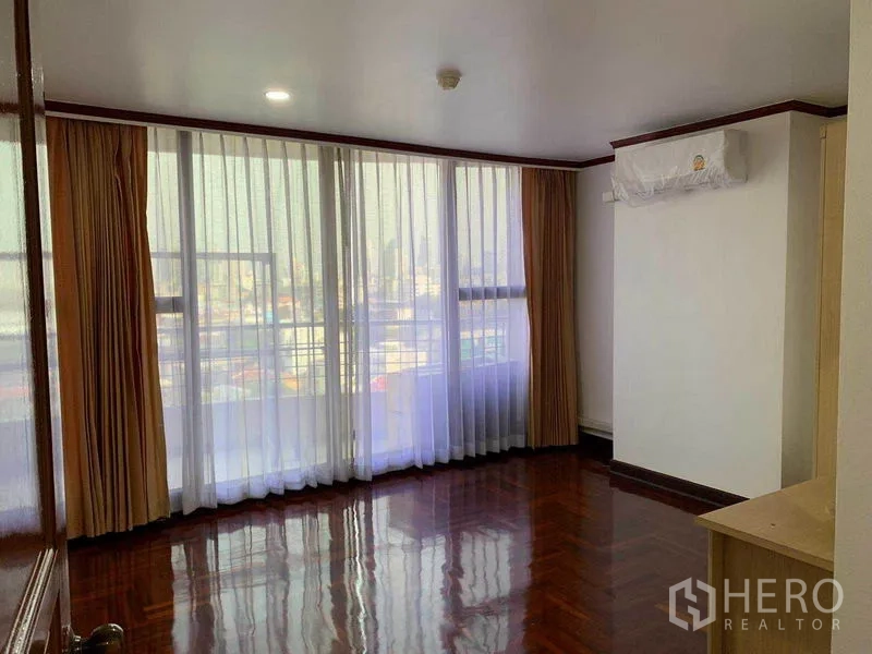 Condominium for rent or sale in Watthana, Bangkok - Second bedroom with floor-to-ceiling windows, polished parquet floors, and a wall-mounted air conditioner.