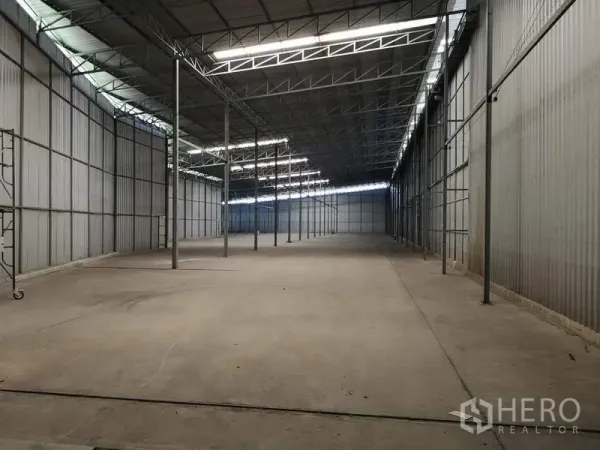 Warehouse for rent in Pak Kret, Nonthaburi - Spacious warehouse interior with a high steel truss roof, skylights, and open concrete floor.
