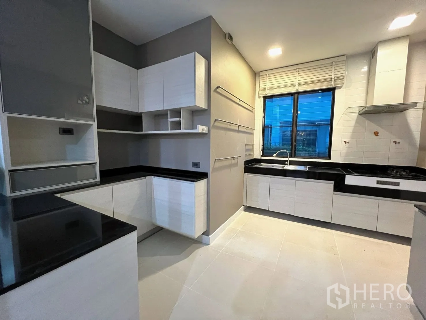 Detached House for rent in Prawet, Bangkok - Modern U-shaped kitchen with white cabinets, black countertops, window, and range hood.
