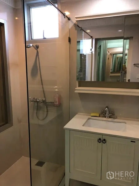 Condominium for rent in Pathum Wan, Bangkok - Modern bathroom with glass-enclosed shower, vanity, and mirrored cabinet.