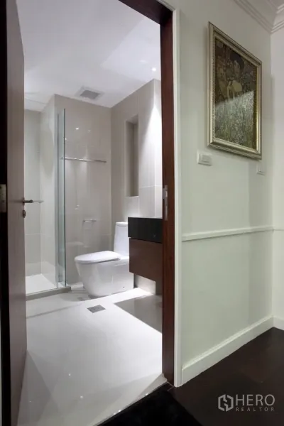 Condominium for rent in Sathon, Bangkok - Modern bathroom with glass-enclosed shower, white tiling, and wall-mounted vanity.