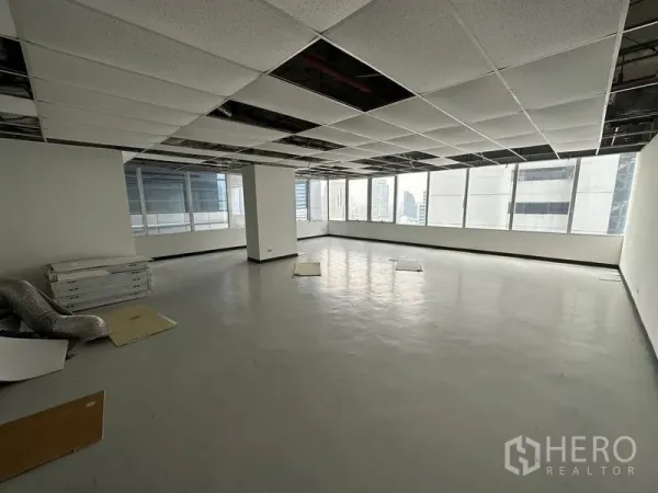 Office Space for rent in Chatuchak, Bangkok - Unfurnished open-plan office interior with suspended ceiling grid partly open, smooth flooring, and large corner windows showing Bangkok city views.