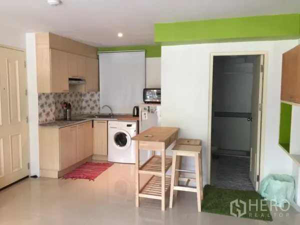 公寓 出租在Khlong Toei, Bangkok - L形浅色木质厨房，带洗衣机、吧台和高脚凳，花纹防溅板。