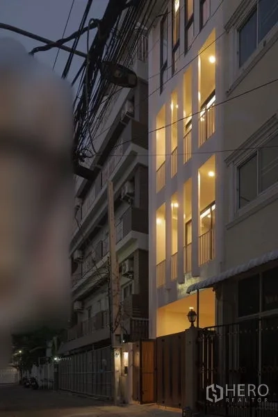 联排别墅 出租 - 黄昏时分的四层联排外立面，竖向窗带灯光，位于安静小巷