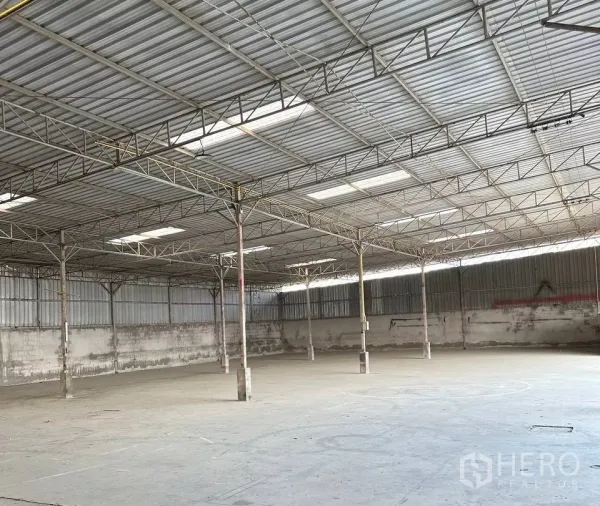 Factory for rent in Samut Prakan - Expansive warehouse hall with high steel truss roof and skylights.