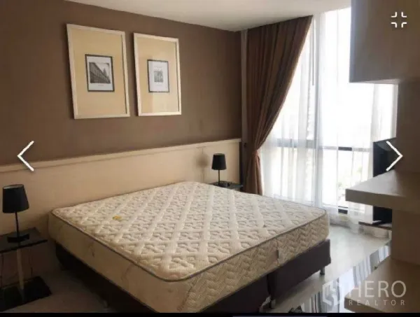 Condominium for rent in Watthana, Bangkok - Master bedroom with large bed, bedside lamps and floor-to-ceiling window with curtains.
