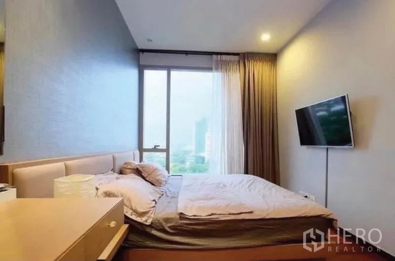 公寓 出售在Khlong Toei, Bangkok - 明亮卧室，城市景观窗，墙挂电视与软包床头。