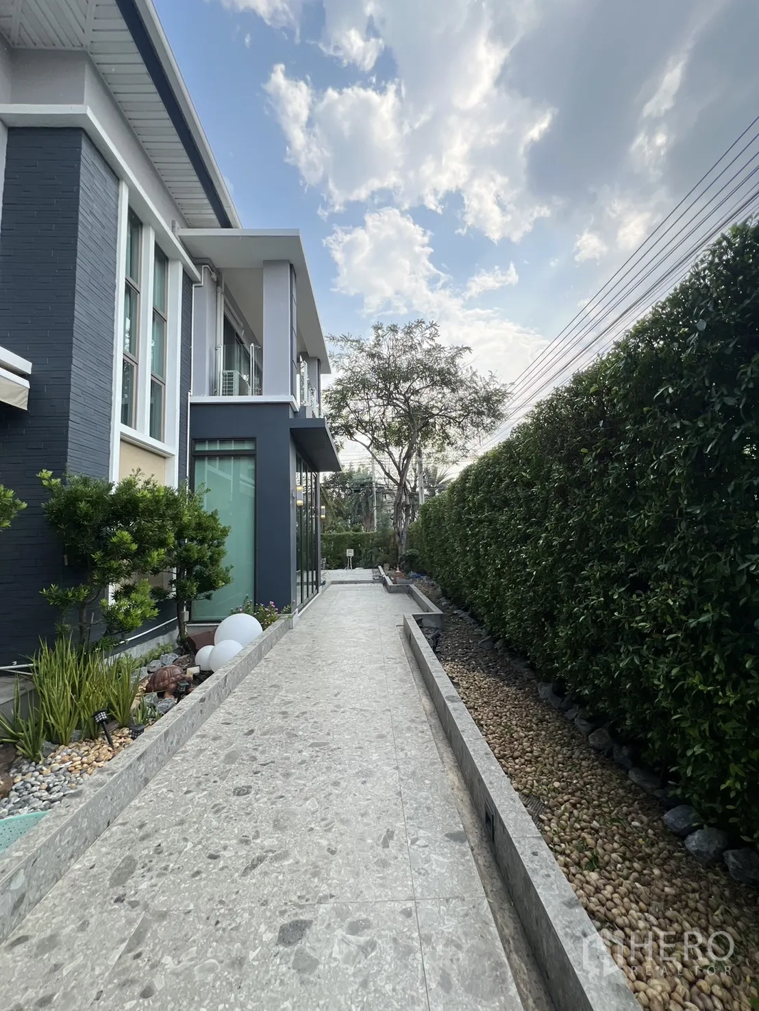บ้านเดี่ยว for rent in Prawet, Bangkok - ทางเดินข้างบ้านเดี่ยวสไตล์โมเดิร์นสองชั้น พร้อมแนวรั้วไม้พุ่มและท้องฟ้าสดใส