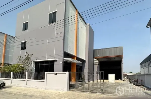 Factory for rent or sale in Lam Luk Ka, Pathum Thani - Street view of modern three-storey factory office with gated driveway and loading area.