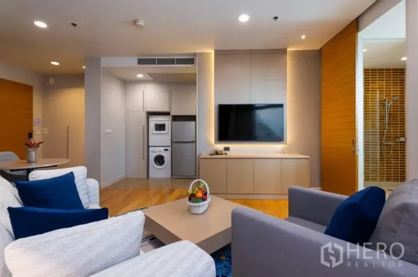 Condominium for rent in Bang Kho Laem, Bangkok - Cozy living area with sofa set, wall-mounted TV, wood floors, and a view toward the laundry niche and bathroom.